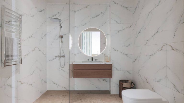 סאנטו אובדיו – גאיה חדר רחצה מודרני עם חיפויי שיש, מקלחת זכוכית ומראה עגולה מוארת.